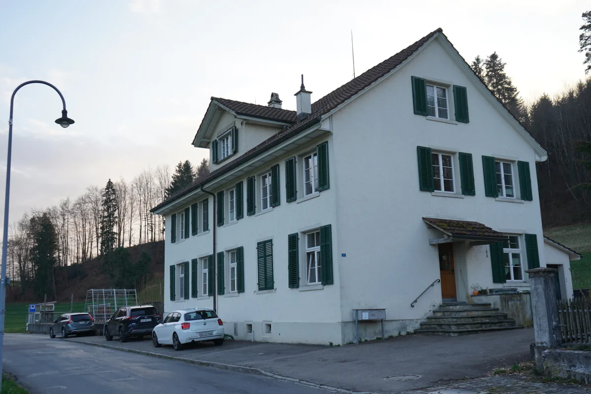 Das alte Schulhaus in Neschwil von aussen, davor stehen einige Autos.